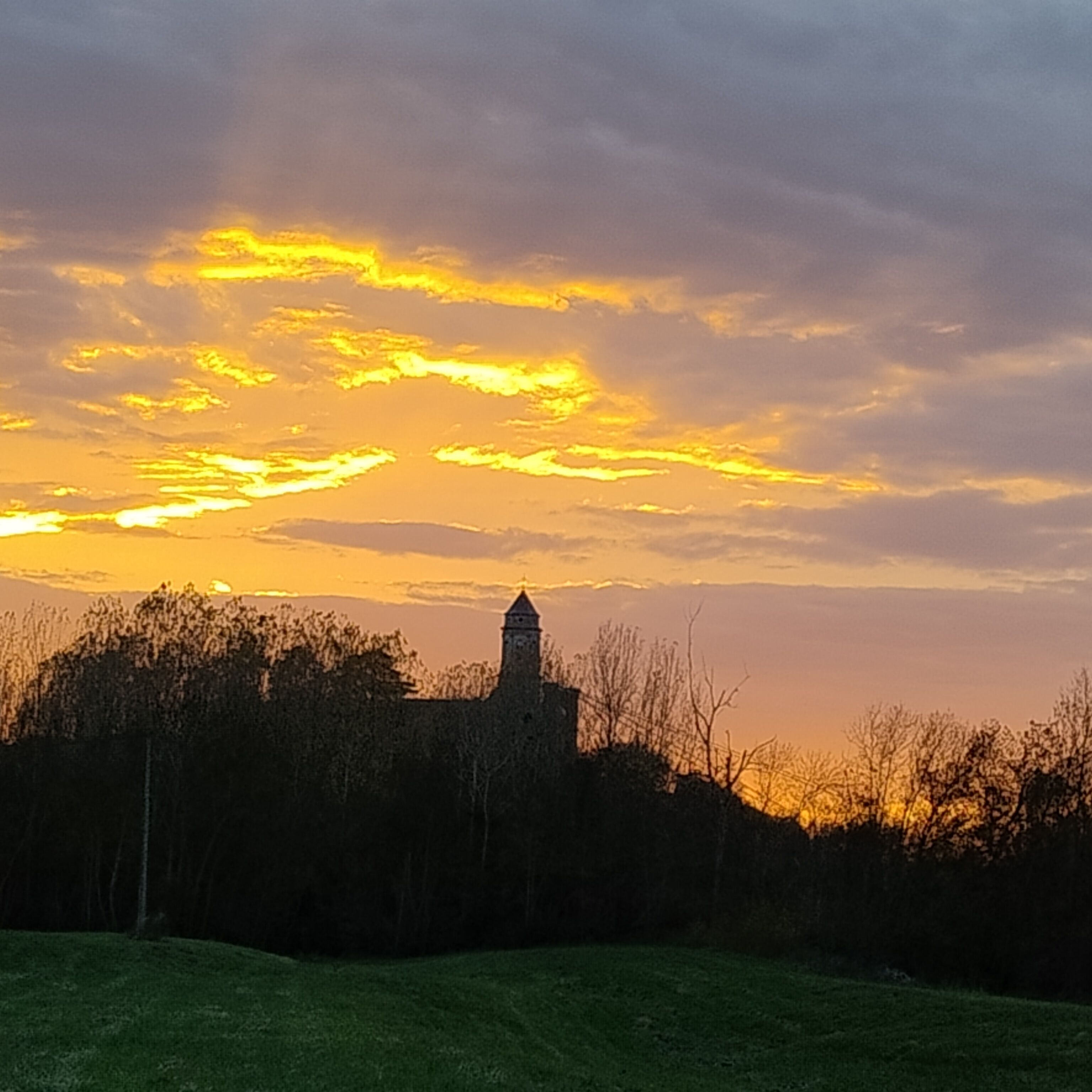 Ein Sonnenuntergang über einem Wiesenfeld, im Hintergrund ein Turm.