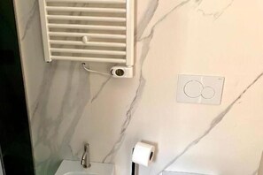 A bathroom with a marble wall, a white radiator, a toilet, and a paper towel dispenser. - Alma Suites (Catania)
