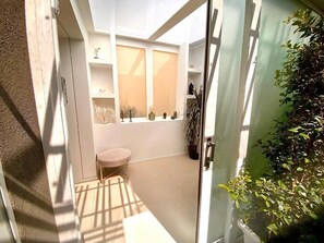 A narrow hallway with a glass door leading to a balcony with a small stool and potted plants.