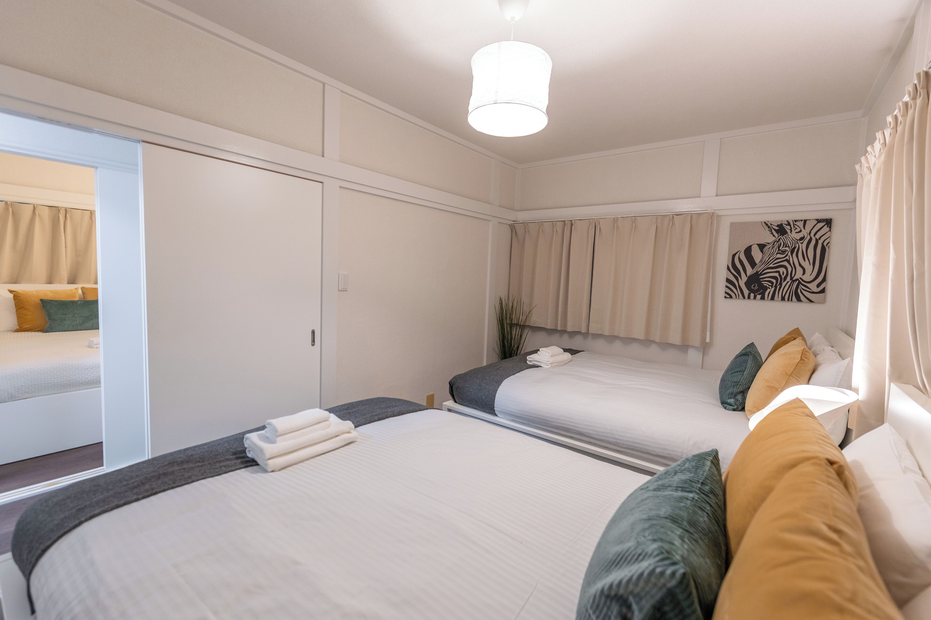 A hotel room with two beds, a large mirror, a zebra artwork on the wall, and a ceiling light.
