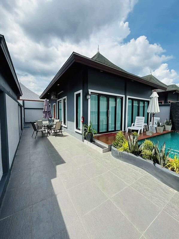 Un edificio moderno con piscina, mobiliario exterior y un patio cubierto.