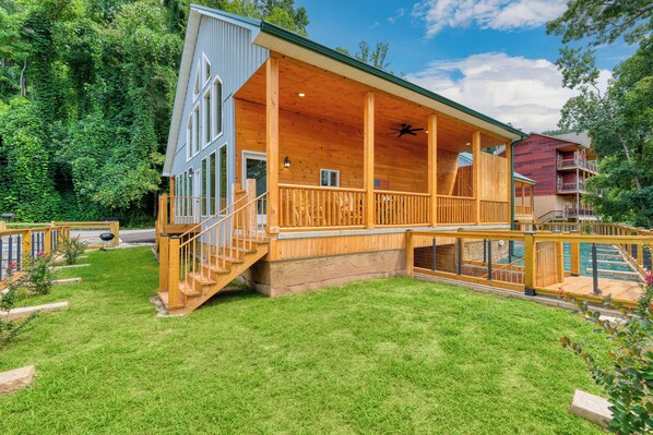 A two-story wooden cabin with a covered porch, a small deck, and a pool area.
