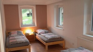 A small, cozy room with two wooden beds, a nightstand, and a window providing a view of the outdoors. - Ferienhaus König - Large house for a large family (Kulmain)