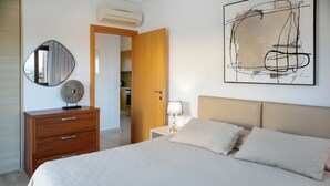 A bedroom with a bed, a dresser, a mirror, a lamp, and a painting on the wall. - 1 Bedroom Apartment - BH12, Aphrodite Hills Rentals – Apartments (kouklia)