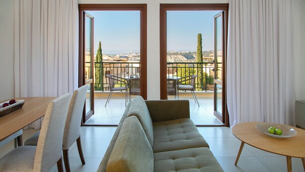 A modern living room with a sofa, chairs, a dining table, and a balcony with a view. - 1 Bedroom Apartment - BH12, Aphrodite Hills Rentals – Apartments (kouklia)
