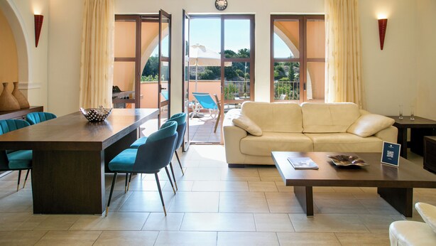 Amplia sala de estar con mesa de comedor, sillas azules, un sofá color beige y un balcón con vistas.