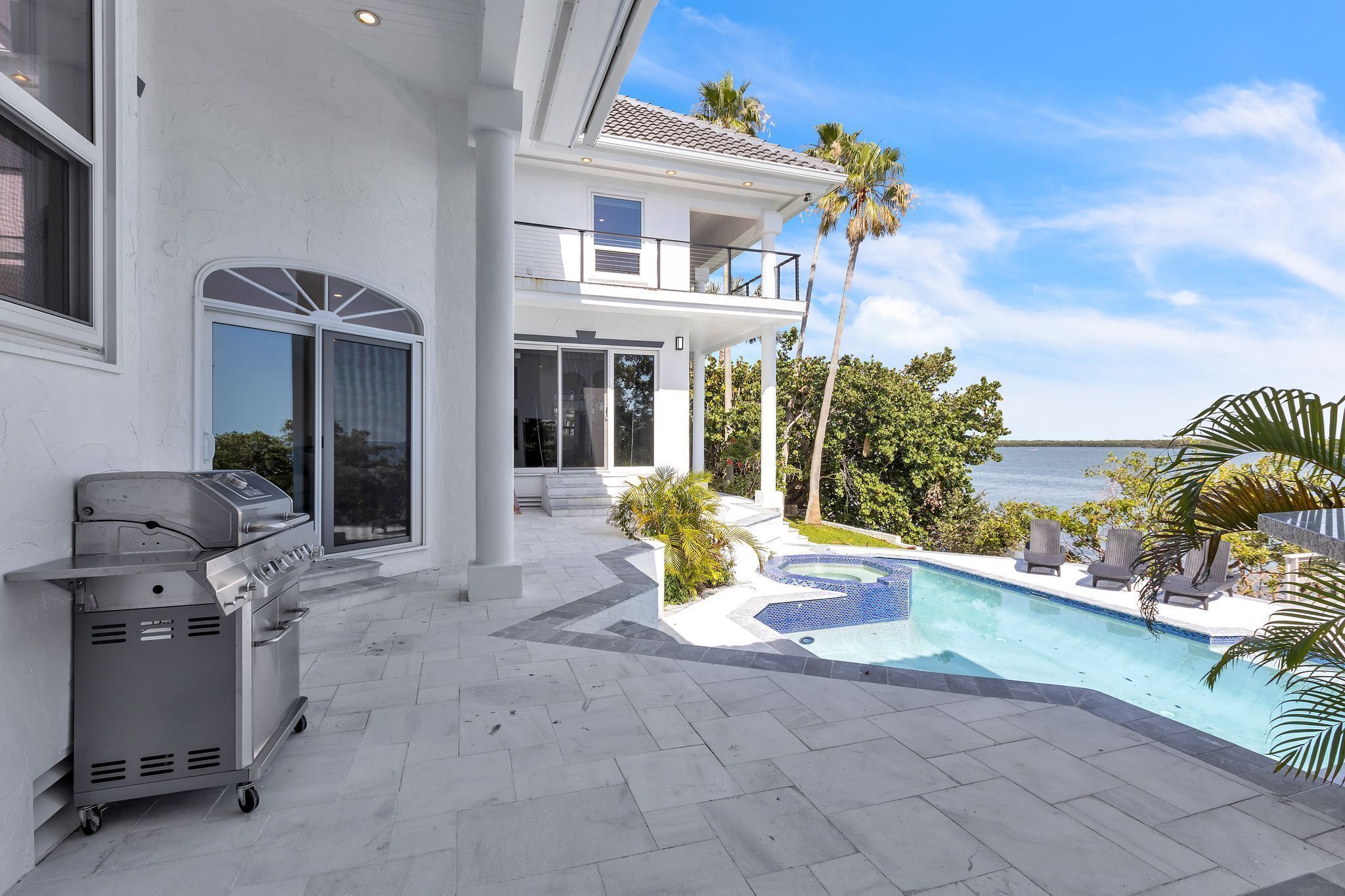 A modern house with a large pool, outdoor grill, and a balcony overlooking the ocean.