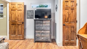 A room with a wooden door, a television on a dresser, and a window with a view of trees. - Stockyards Longhorn House, 1/8 mi to Stockyards-Sleeps up to 11-add 10 next door (Fort Worth)