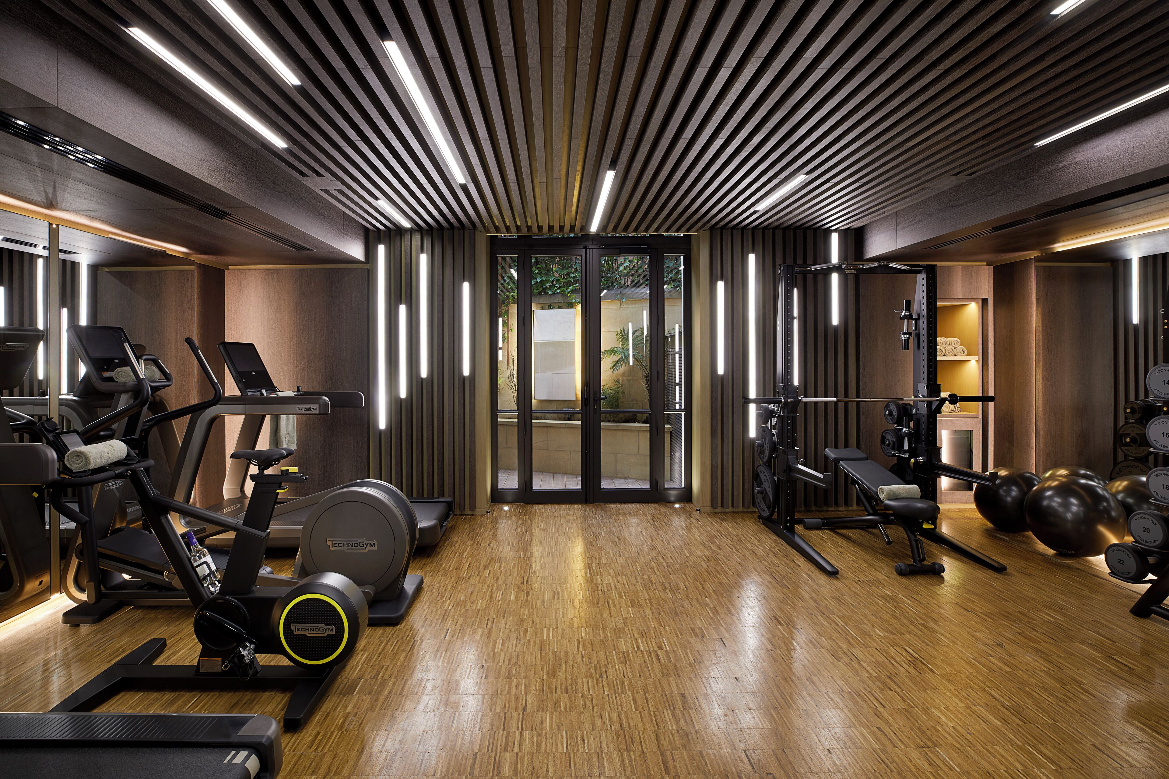 A modern gym with exercise equipment, wooden flooring, and a contemporary ceiling design.