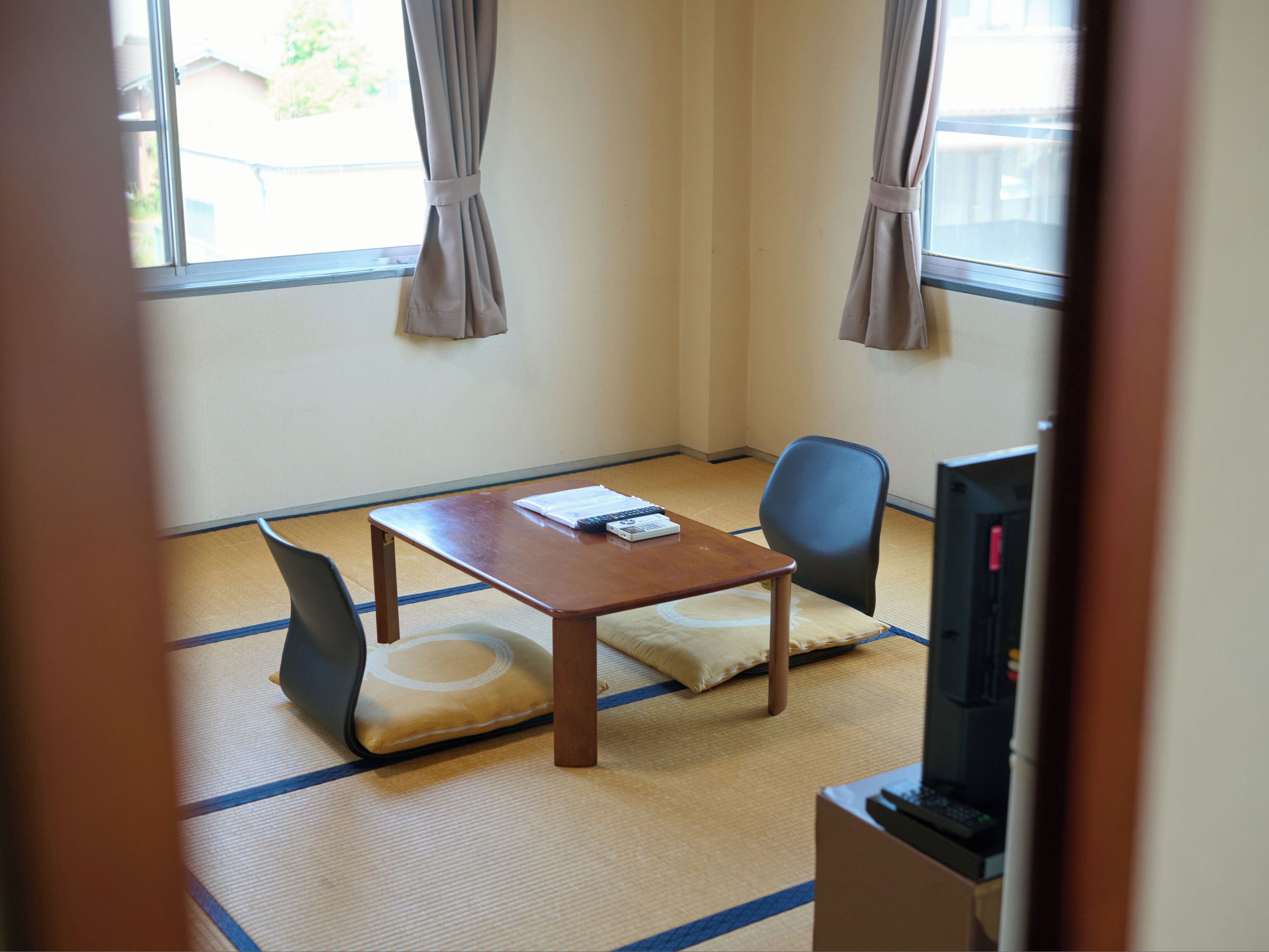 Una habitación con suelo de tatami, una mesa de madera, dos sillas, un televisor y una ventana con cortinas.