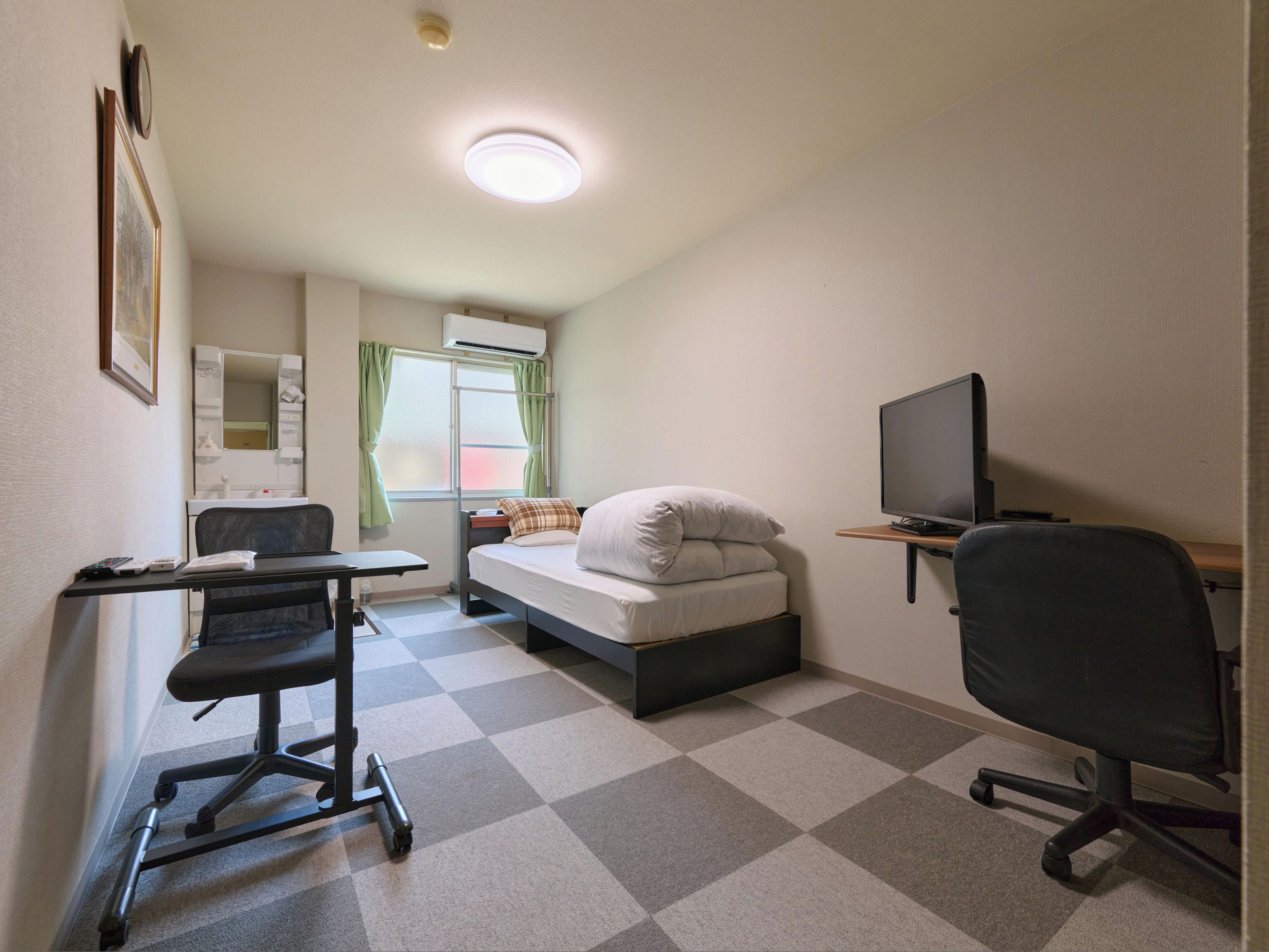 A compact hotel room with a bed, a desk with a chair, a television, and a window with curtains.