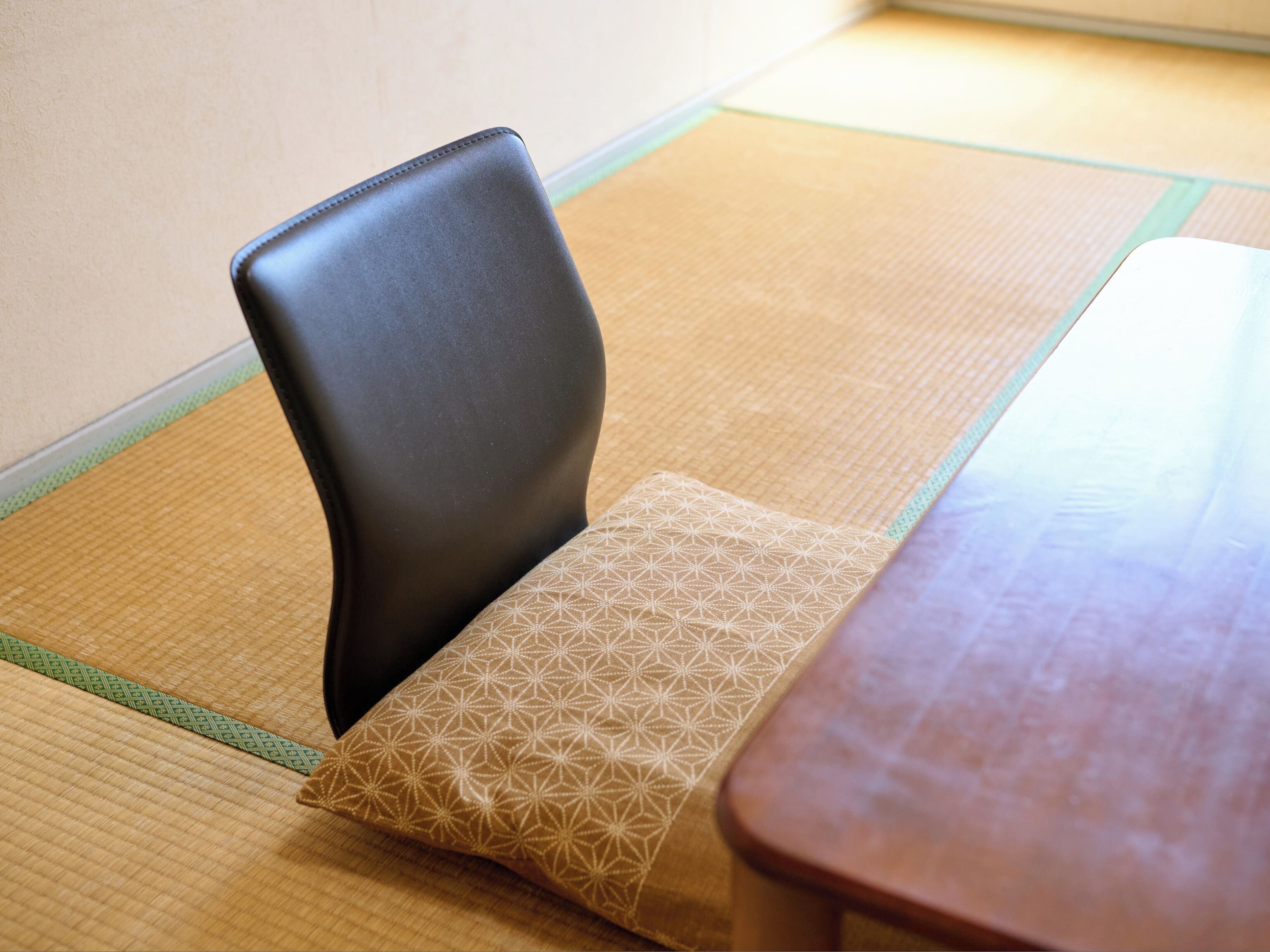 A tatami mat floor with a wooden table and a black chair with a patterned cushion.
