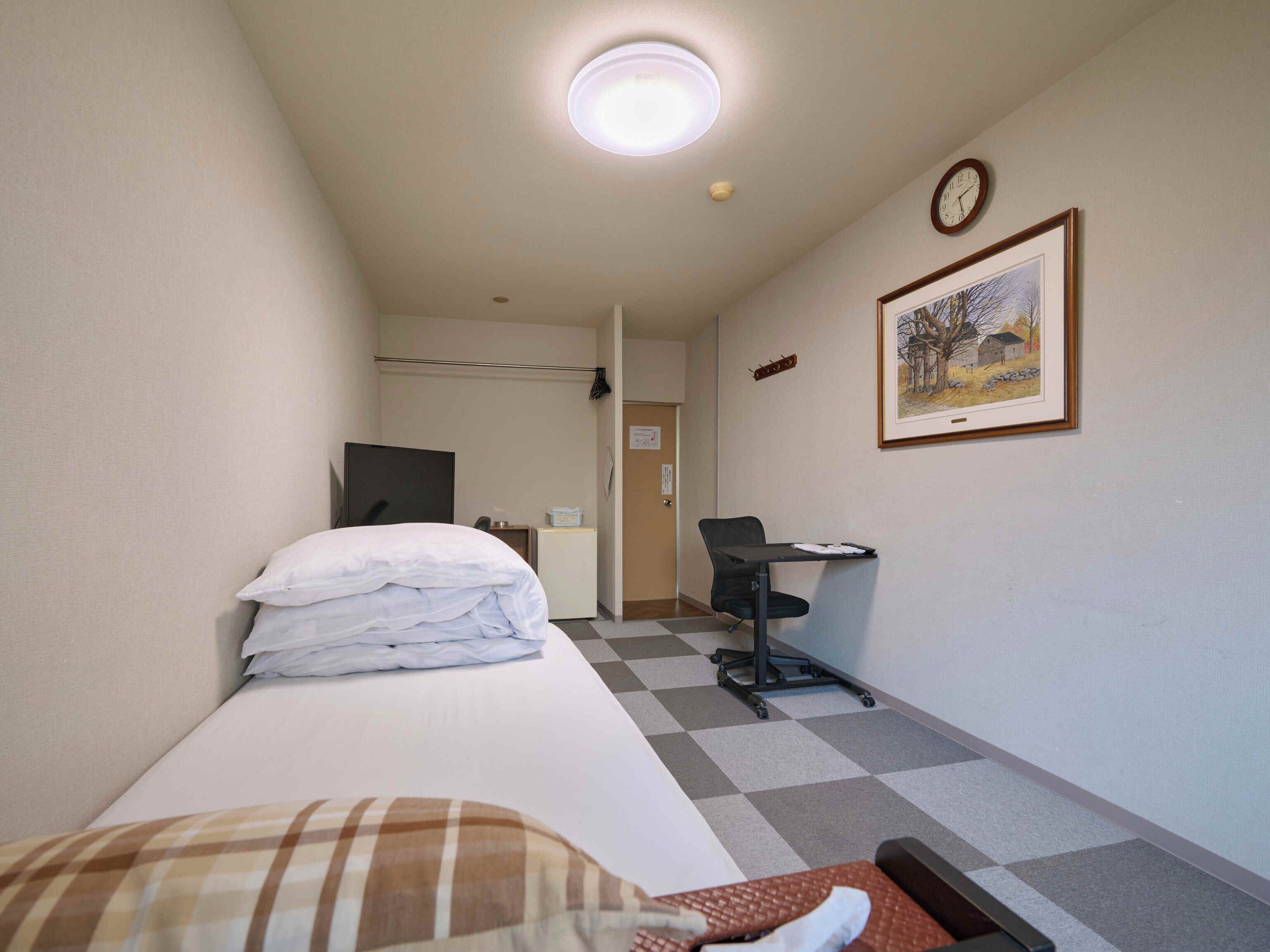 A hotel room with a bed, a desk, a chair, a clock, and a framed picture on the wall.
