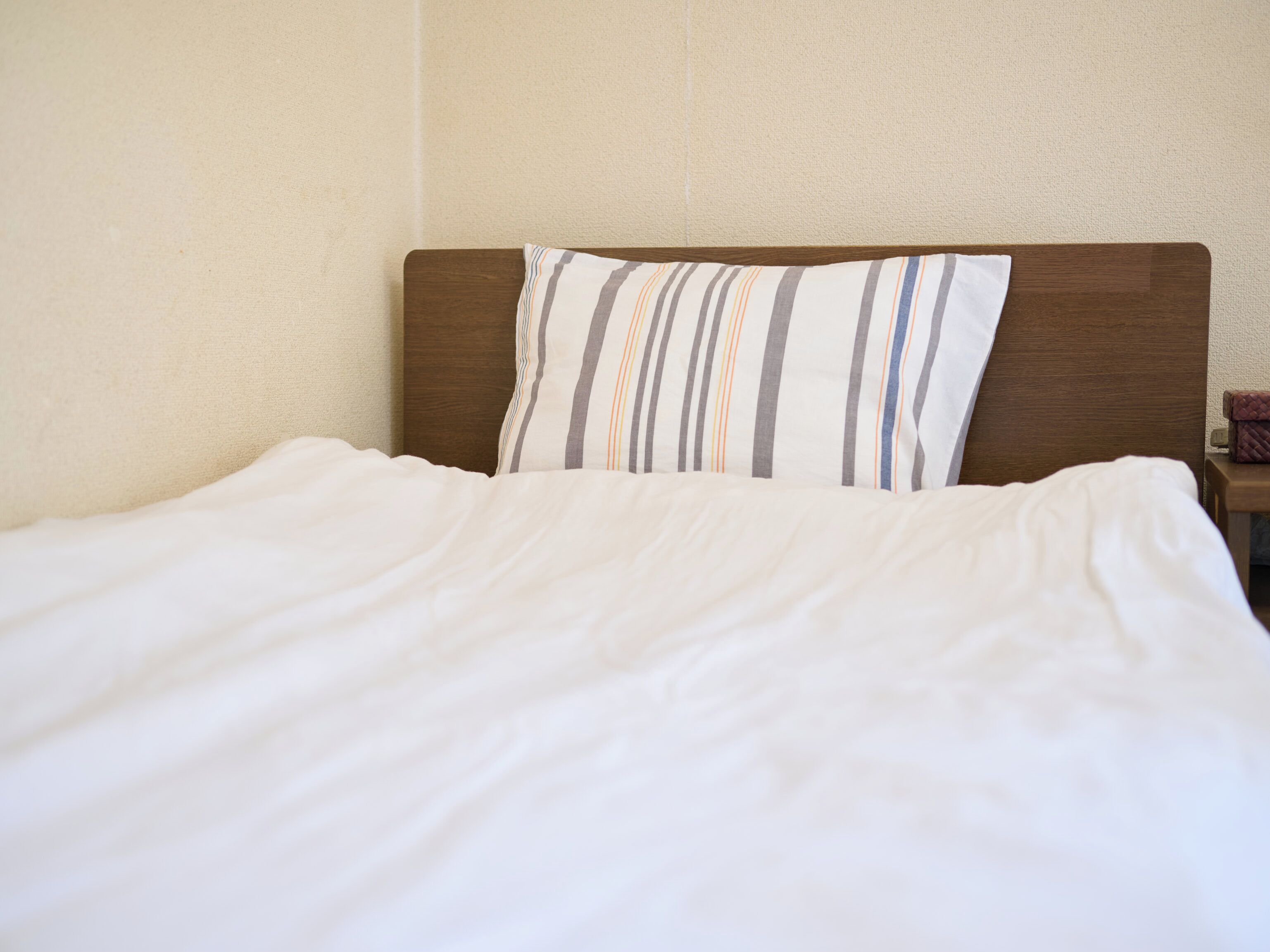A neatly made bed with a striped pillow and a wooden headboard.