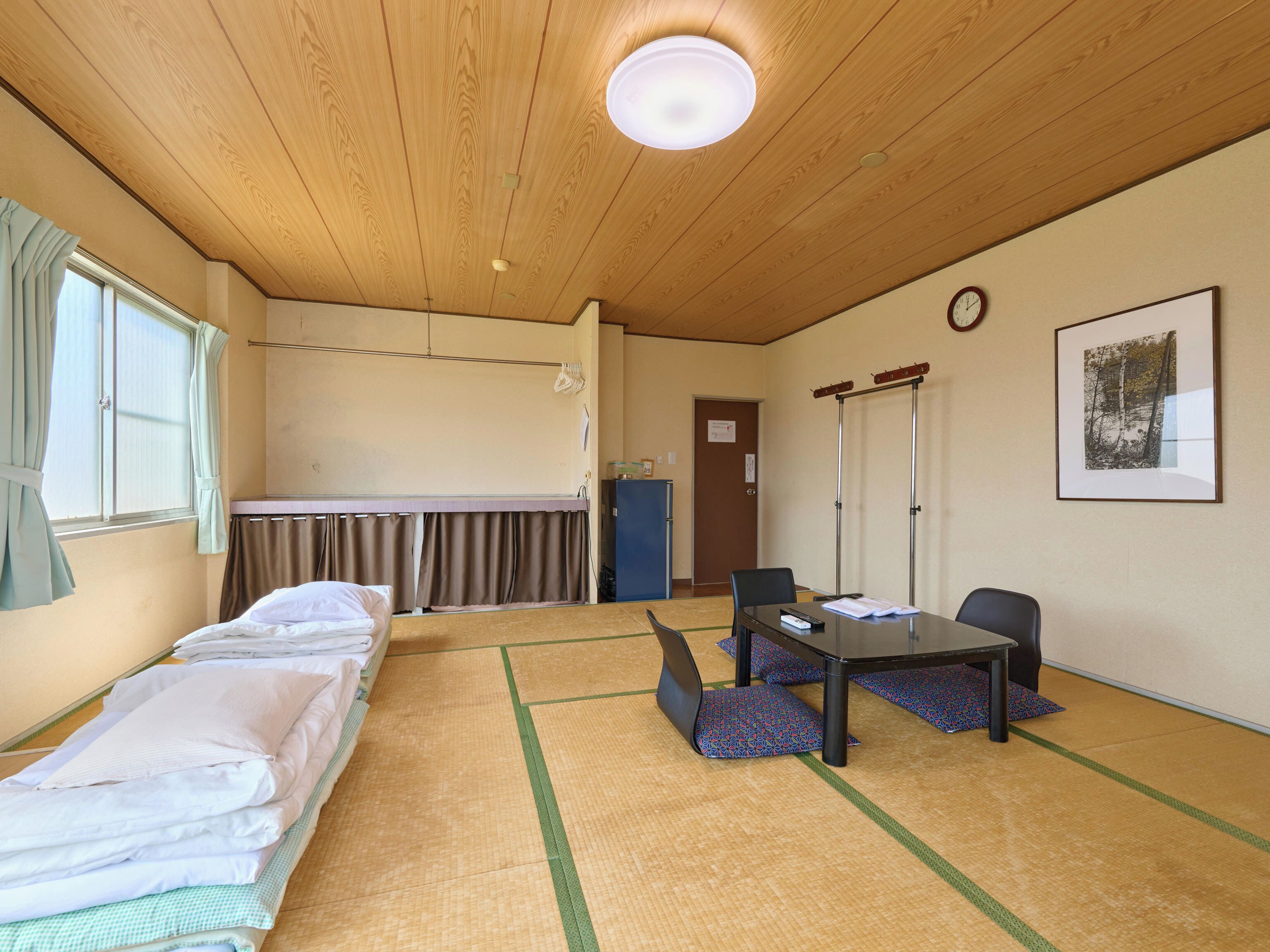 A room with a wooden ceiling, a bed, a table with chairs, a clock, and a framed picture on the wall.