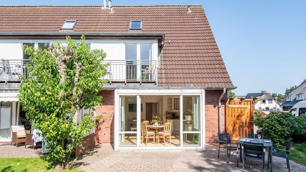 A two-story house with a brick facade, a tiled roof, and a glass door leading to a patio with outdoor furniture. - Huus Lerchenkoje 2 - Huus Lerchenkoje (Sylt)