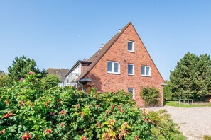 Une maison en briques rouges, avec un toit triangulaire, de nombreuses fenêtres et un petit porche.