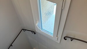 A spiral staircase with a small window at the top, white walls, and black handrails. - L'OUSTAU DE FLAYOSC (Flayosc)