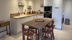 A modern kitchen with white cabinetry, a wooden dining table, and a built-in oven. - L'OUSTAU DE FLAYOSC (Flayosc)