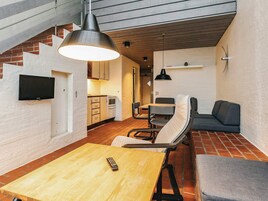 Un espacio habitable compacto con zona de comedor, sofá, televisión montada en la pared y cocina al fondo.