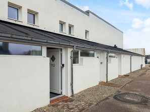 A row of white buildings with numbered doors, a gravel path, and a manhole cover. - 6 Person Holiday Home in Brovst (Brovst)