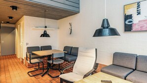 Un intérieur moderne avec un sol en briques, un plafond en bois et un mélange de meubles gris et blancs, notamment un canapé, un fauteuil et une table.