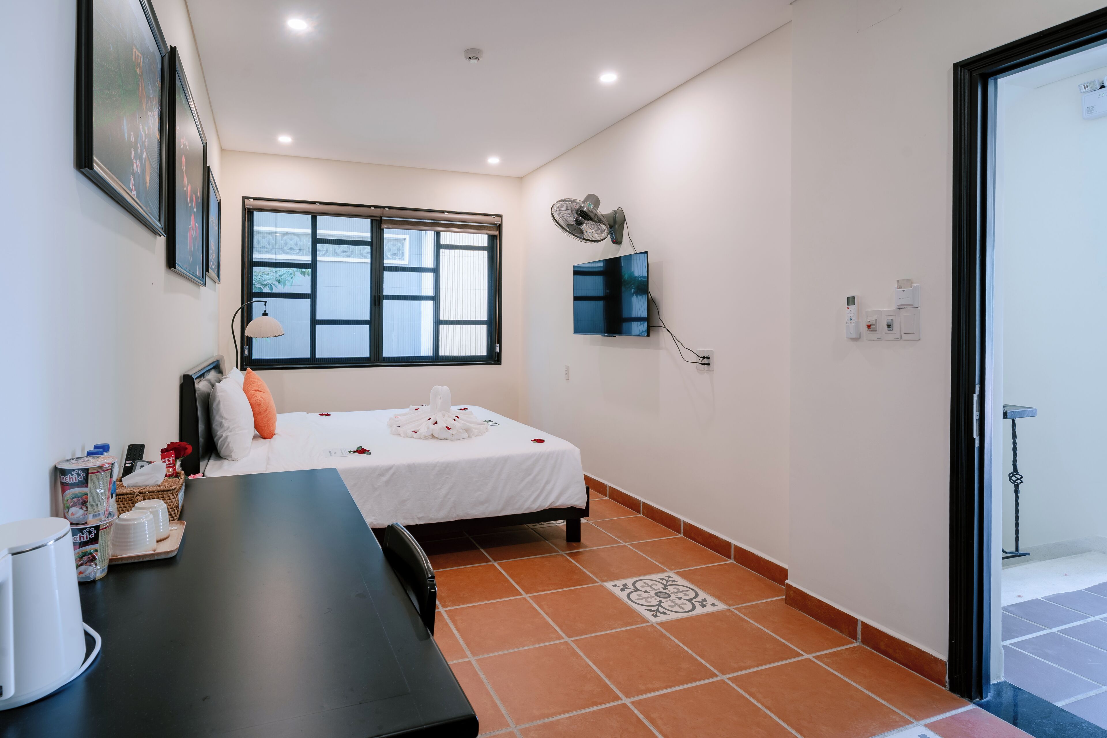 A hotel room with a bed, a desk, a chair, a window, a wall-mounted TV, and a door.