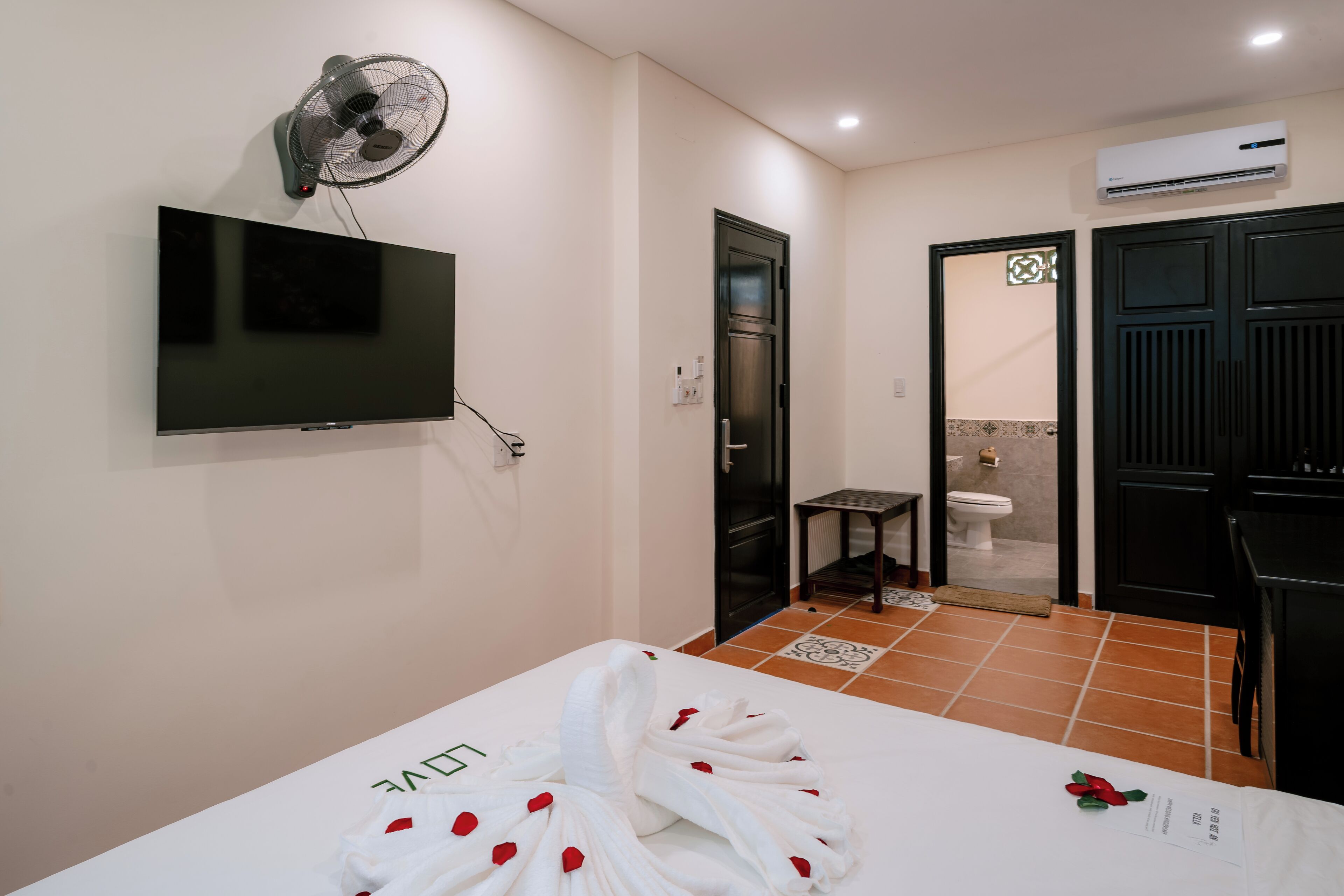 A hotel room with a bed, a TV, an air conditioner, and a bathroom.