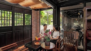 A cozy indoor seating area with wooden furniture and a table with a vase and drinks. - Du Yen Hoi An Villa (Da Nang)
