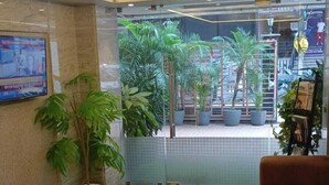 Un hall d’entrée agrémenté d’un lustre, de plantes en pot, d’un comptoir de réception et d’un espace salon.
