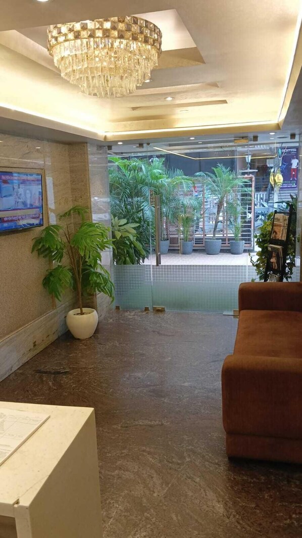 Un vestíbulo con candelabro, plantas en macetas, mostrador de recepción y zona de estar.