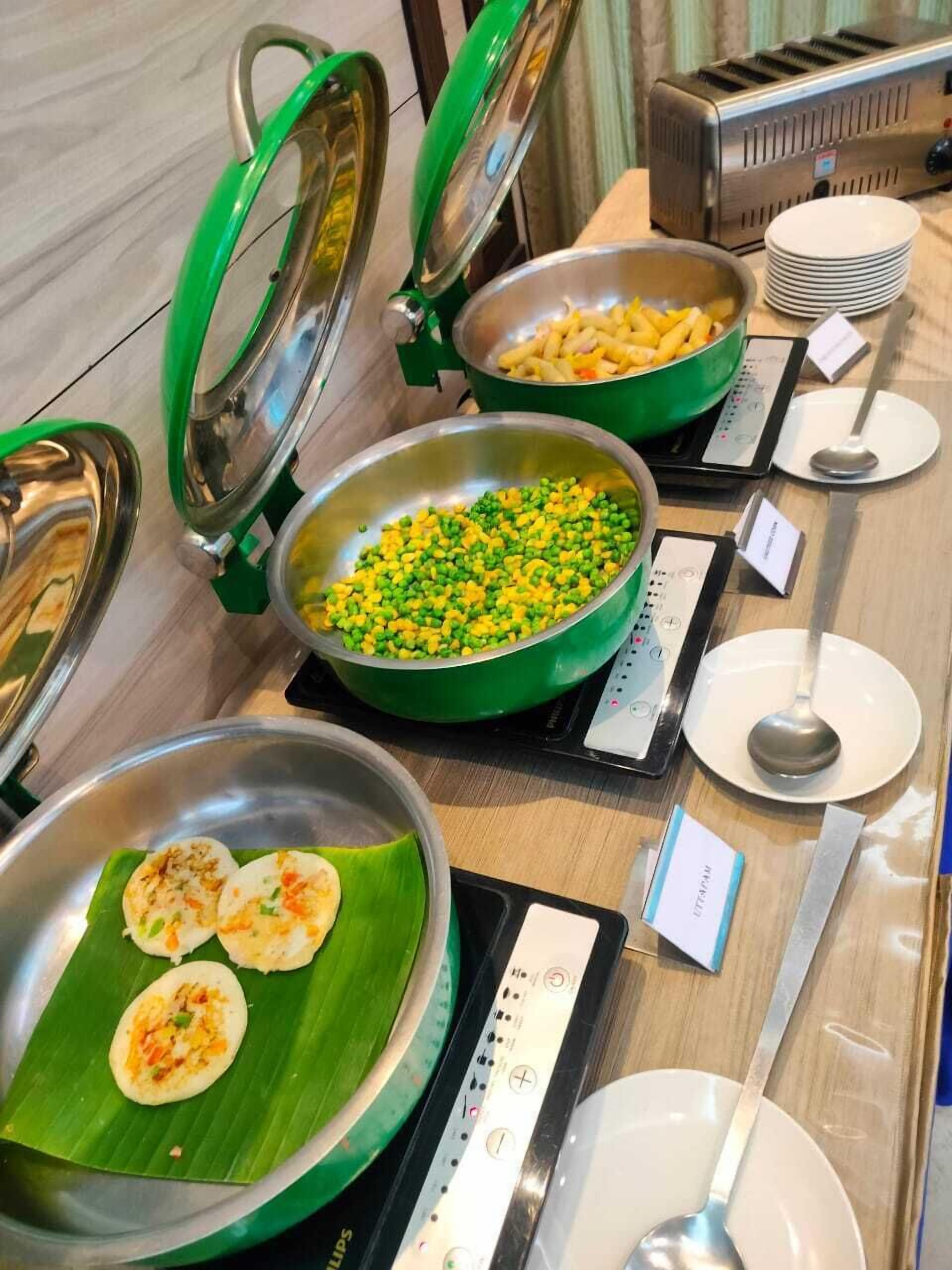 Montaje tipo bufé con diferentes opciones de comida, incluyendo un tazón de vegetales mixtos, un plato de idlis y un tostador.