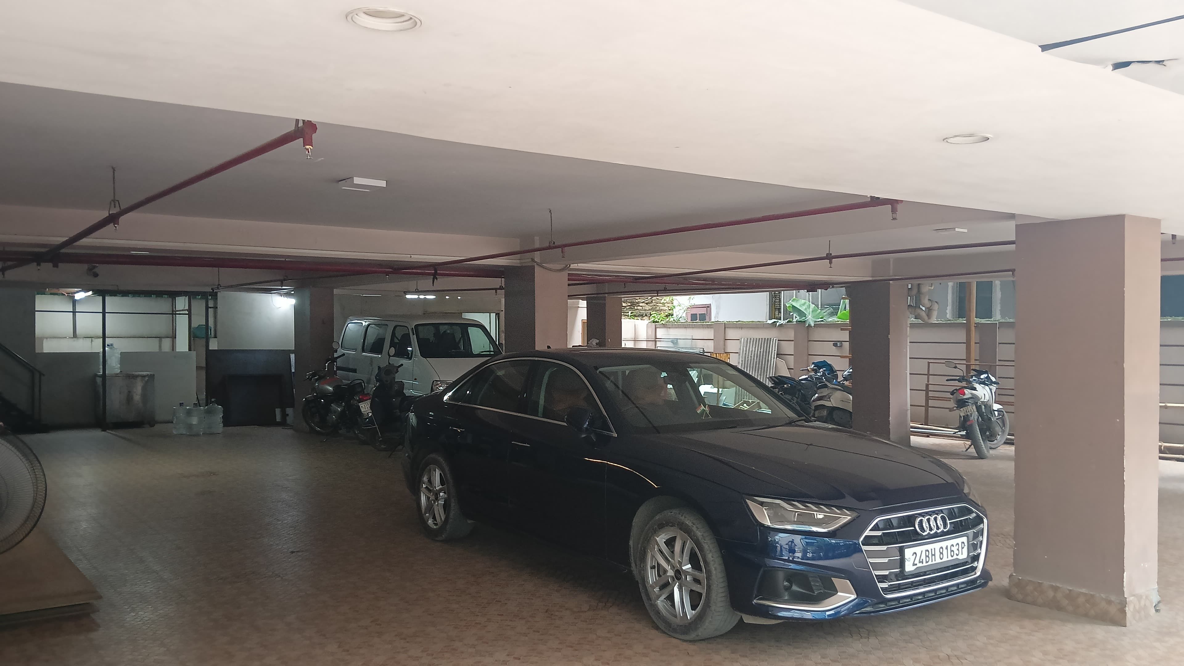 Un estacionamiento con un automóvil negro, una camioneta blanca y una motocicleta.