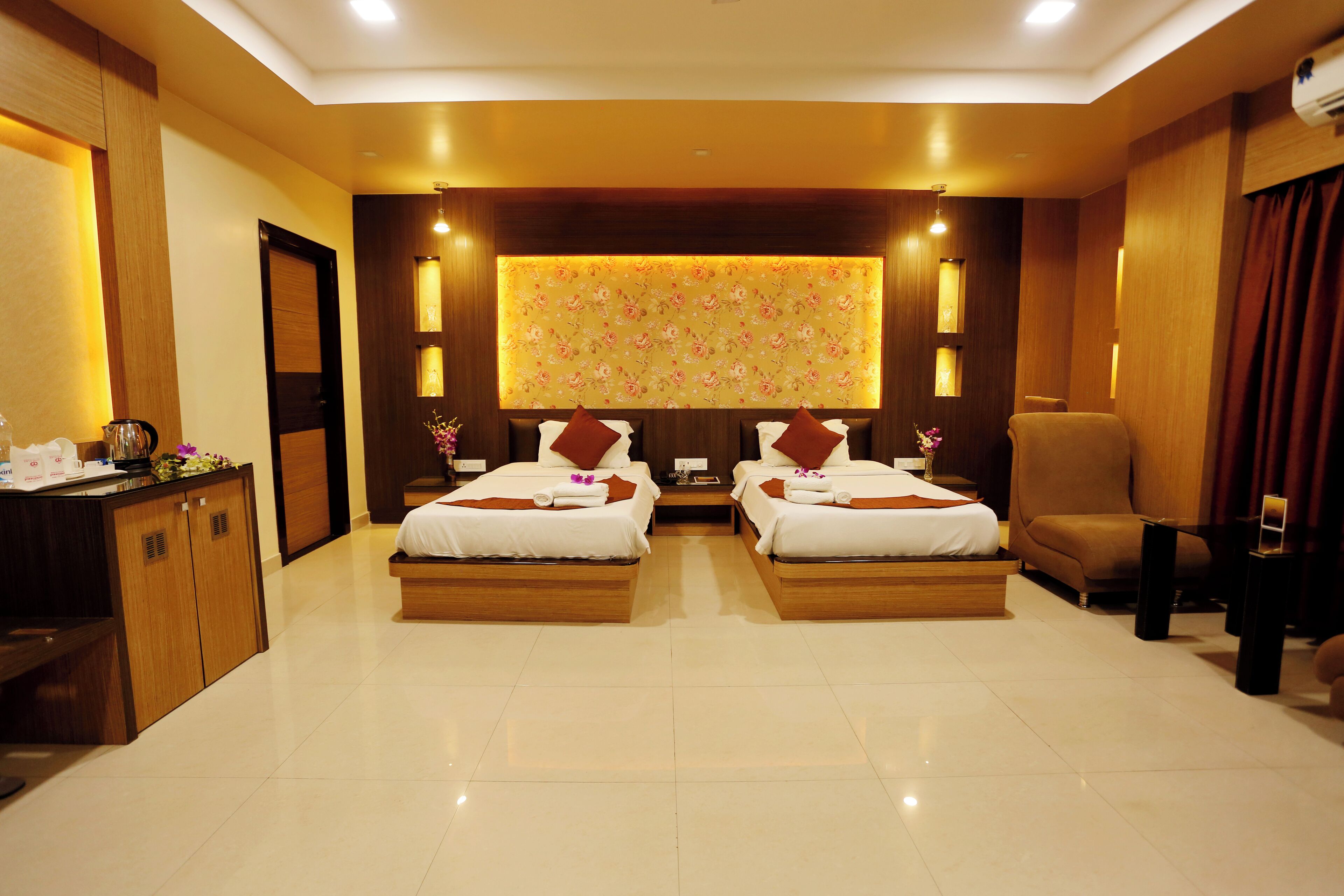 A hotel room with two beds, a desk, a chair, and a large floral-patterned wall.