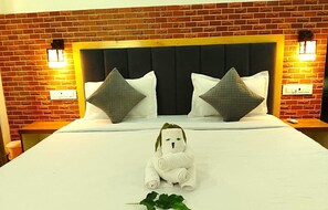 Et hotelværelse med en væg i murstensmønster, en træsengegavl, to puder, et hvidt sengetæppe og en lille hvid bamse på sengen.