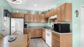 A kitchen with wooden cabinets, a white refrigerator, a black microwave, and a dining table with chairs.
