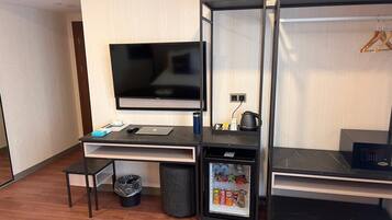 Ein kleines Hotelzimmer mit Flachbildfernseher, einem kleinen Schreibtisch mit Laptop, einem Kühlschrank und einem Mülleimer.