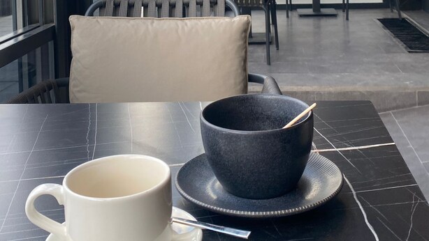 Een modern zithoekje binnen met een tafel, stoelen en een groot raam met uitzicht op de straat.