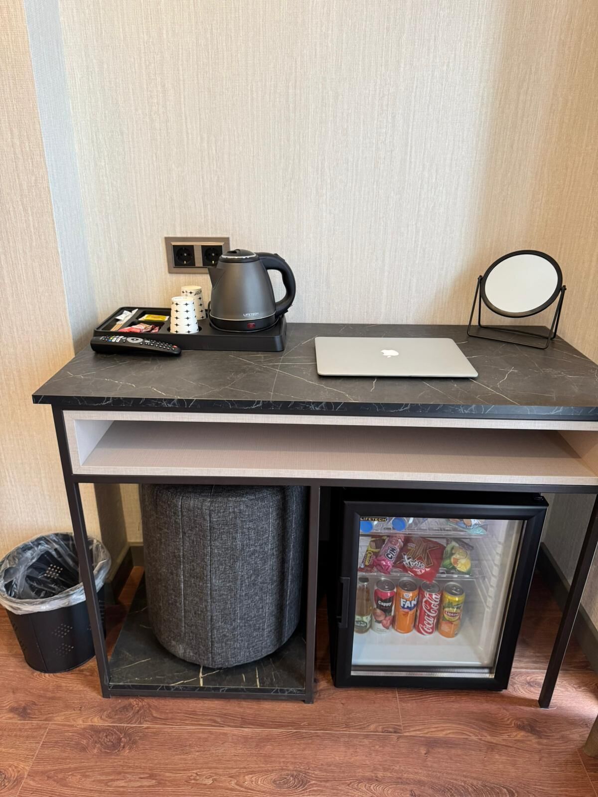 Espacio de trabajo compacto con una computadora portátil, un hervidor de agua y un refrigerador pequeño con bebidas.
