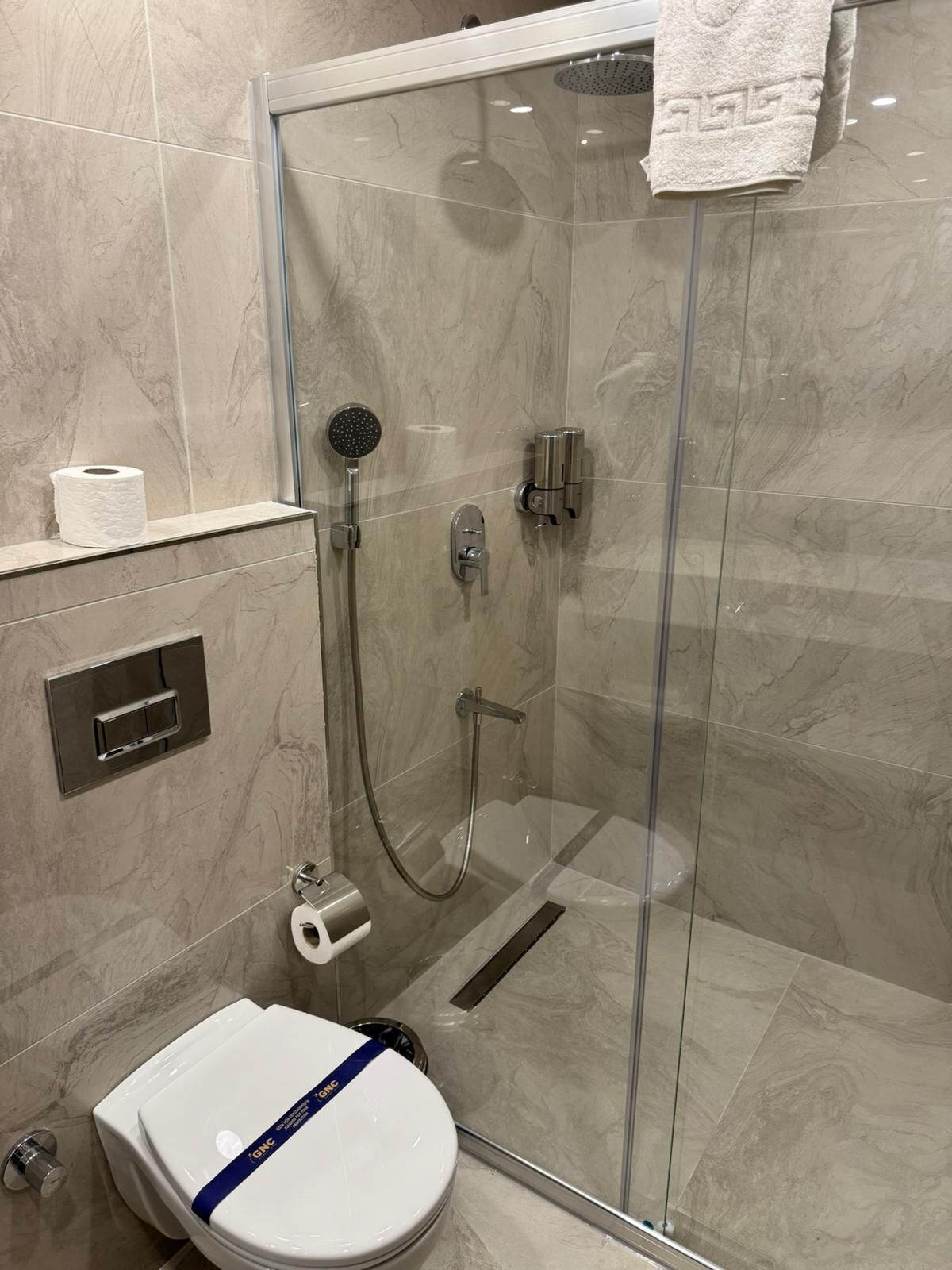 A modern bathroom with a glass-enclosed shower, a toilet, and a paper towel dispenser.