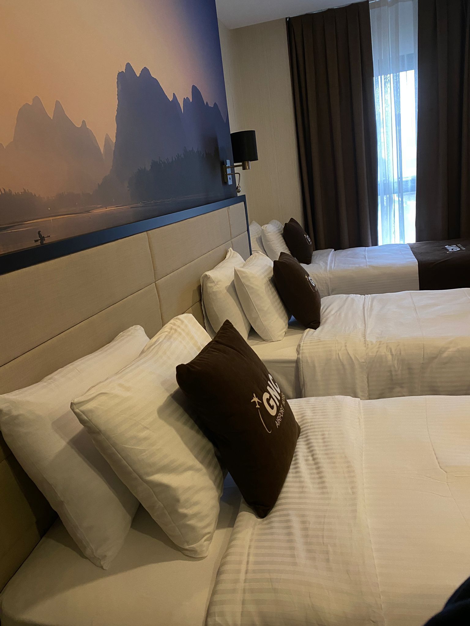 Habitación de hotel con dos camas, cada una con ropa blanca y una almohada marrón con el logotipo 