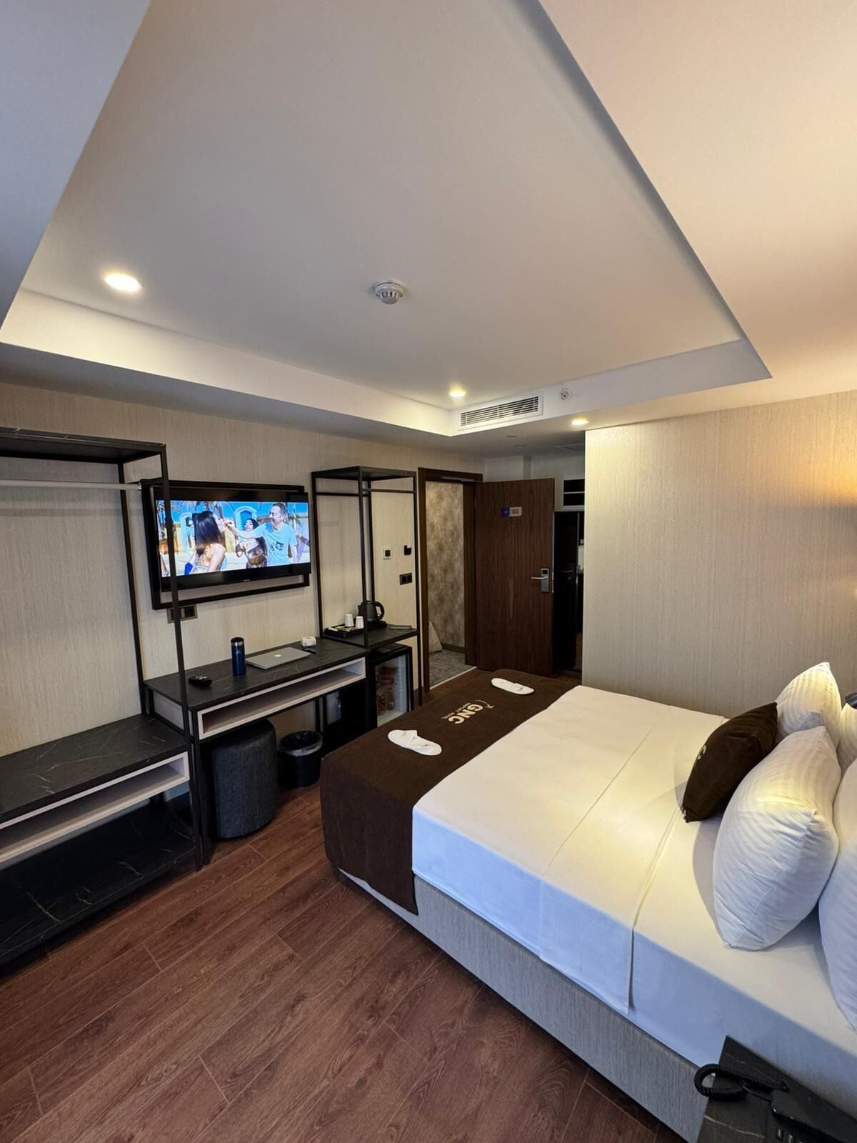 A modern hotel room with a bed, a TV, a desk, and a wardrobe.