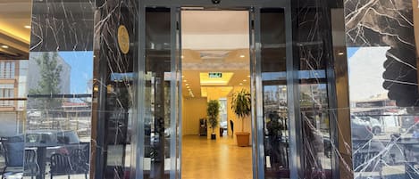 A hotel entrance with a red carpet, glass doors, and a view of the interior.