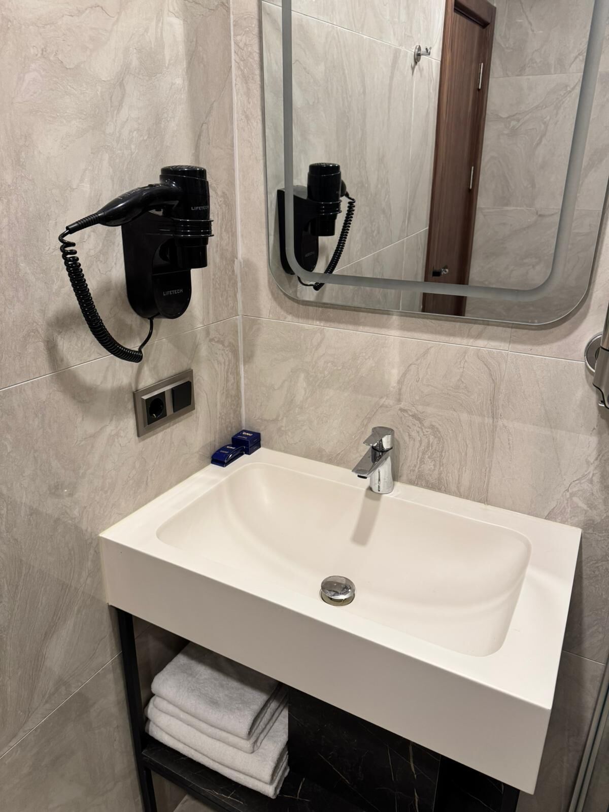A bathroom with a white sink, a mirror, and a hairdryer mounted on the wall.