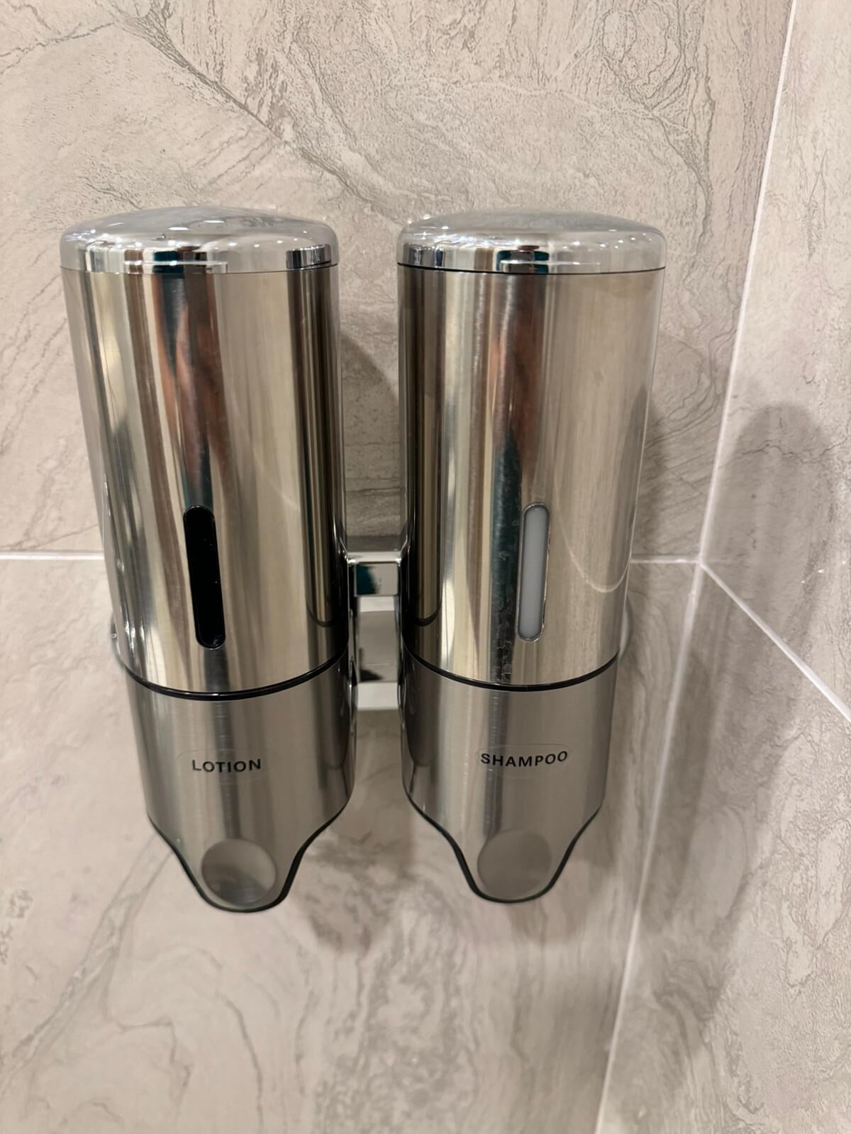 A bathroom with two metallic dispensers labeled 'LOTION' and 'SHAMPOO' mounted on a wall.