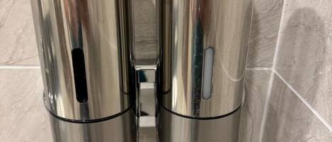 A bathroom with two metallic dispensers labeled 'LOTION' and 'SHAMPOO' mounted on a wall.