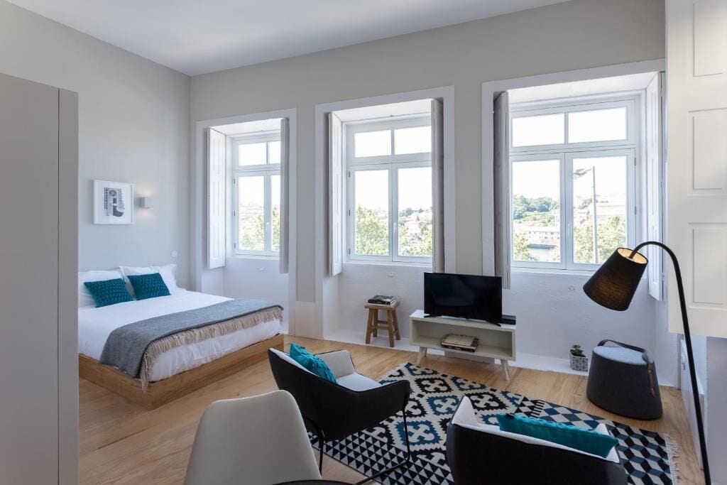 A modern bedroom with a bed, a desk, a TV, and a lamp.