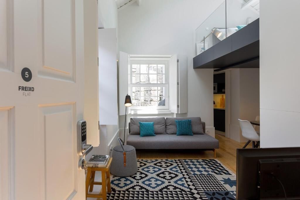 Een moderne woonkamer met een bank, een tapijt met een patroon, een lamp en een deur met de tekst 'FREIXO FLAT'.