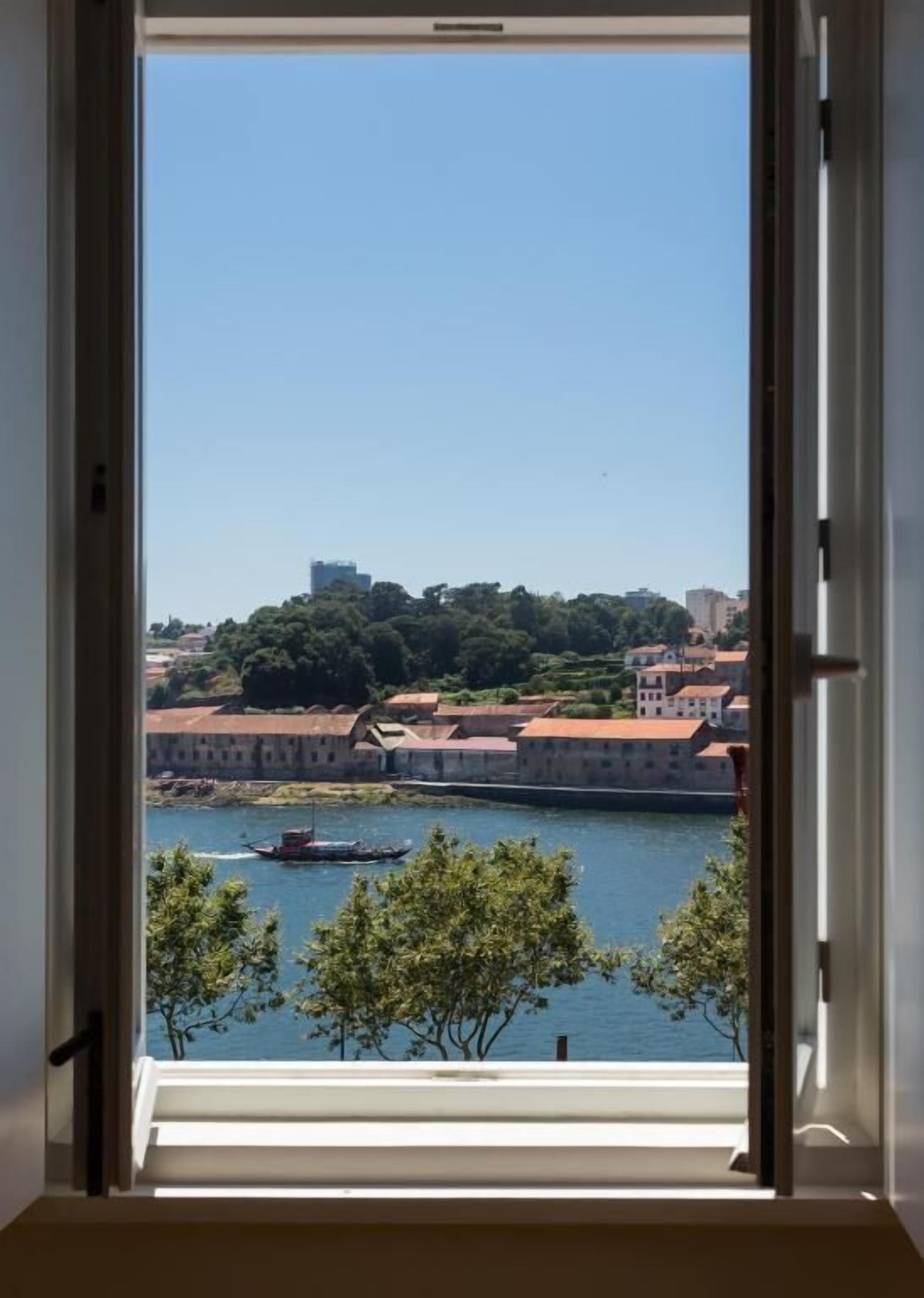 A view through a window of a river with a boat, buildings, and trees.