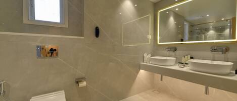 A modern bathroom with a toilet, two sinks, a large mirror, and a window.